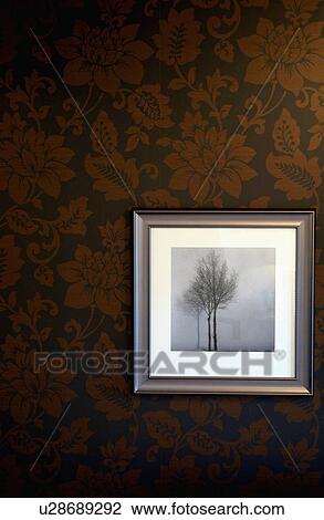 Stock Image - Close-up of framed black and white photograph of a tree on brown patterned wallpaper. Fotosearch