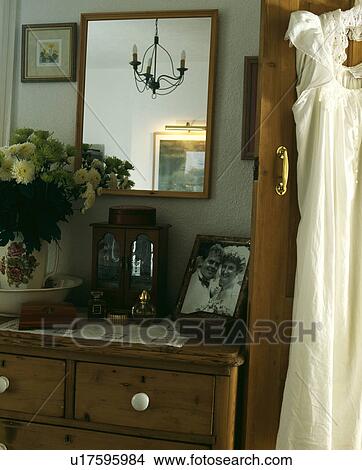 Picture - Close-up of mirror above chest-of-drawers with photograph and yellow chrysanthemums in bedroom. Fotosearch