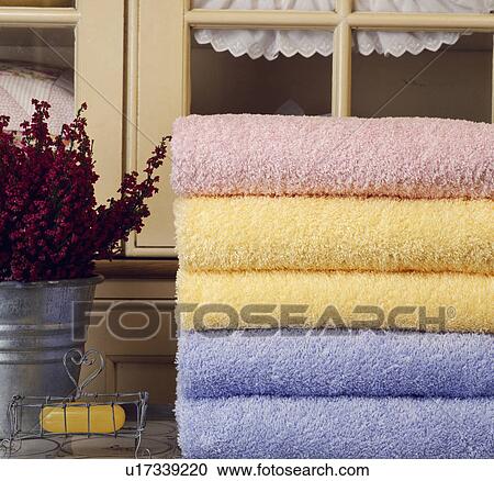 Stock Image - Close-up of pile of pastel coloured bathroom towels beside soap in wirework dish. Fotosearch