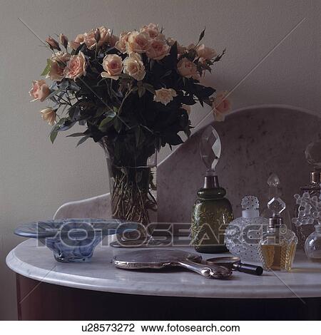 Stock Image - Close-up of pink roses and collection of antique glass perfume bottles. Fotosearch