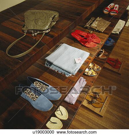 Stock Image - Close-up of shoes and scarves with bags on wooden display shelves in Jigsaw clothes shop. Fotosearch