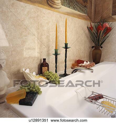 Stock Image - Close-up of soap and seashells on the side of bath with candles in tall candlesticks . Fotosearch