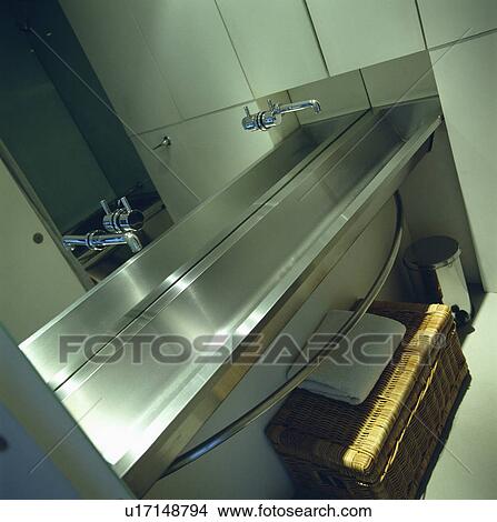 Picture - Close-up of stainless steel taps and long stainless steel basin below mirrored bathroom wall. Fotosearch