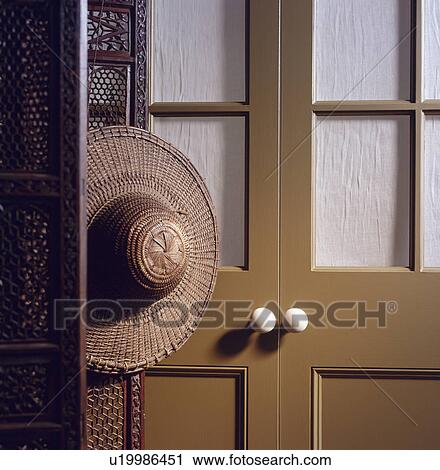 Stock Image - Close-up of straw hat on screen beside brown half-glazed doors. Fotosearch