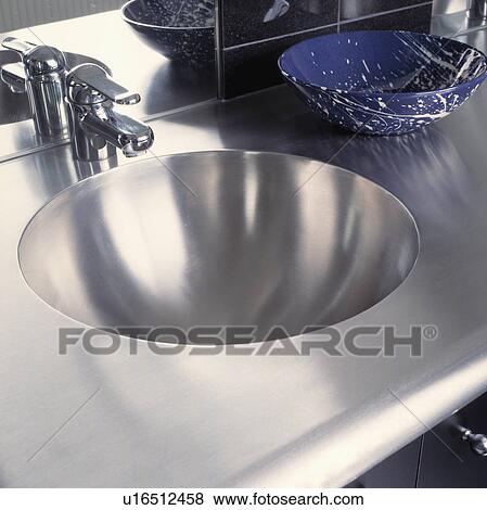 Stock Photo - Close-up of tap and stainless steel circular basin inset in steel vanity unit. Fotosearch