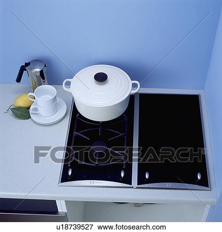 Stock Photo - Close-up of white cups and stainless steel coffee pot beside white Le Creuset pan on black gas dual hob &#13; &#10; &#13; &#10; &#13; &#10; &#13; &#10; &#13; &#10;. Fotosearch