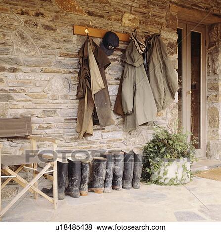 Stock Photo - Coats on stone wall above wellington boots on veranda. Fotosearch