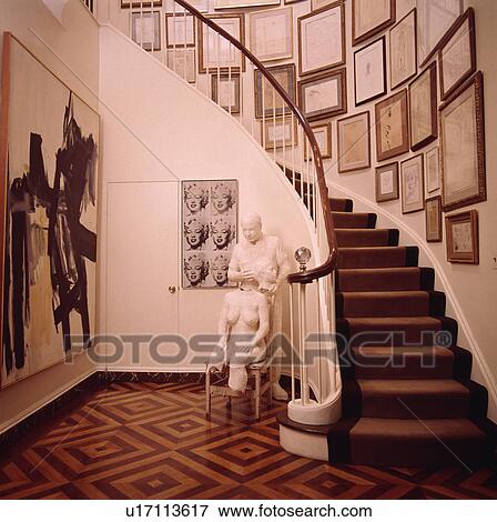 Stock Photo - Collection of pictures above curved staircase with brown carpet in cream hall with sculpture and patterned wood floor. Fotosearch