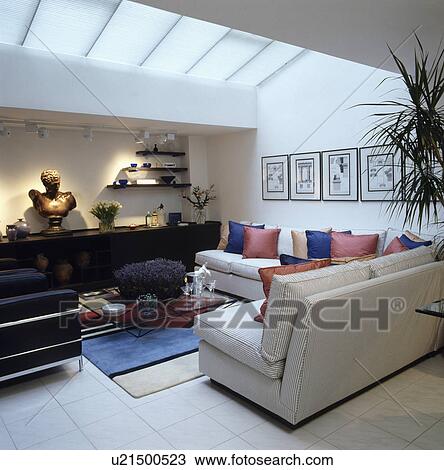 Stock Image - Colourful cushions on white sofas in white loft conversion modern living room. Fotosearch