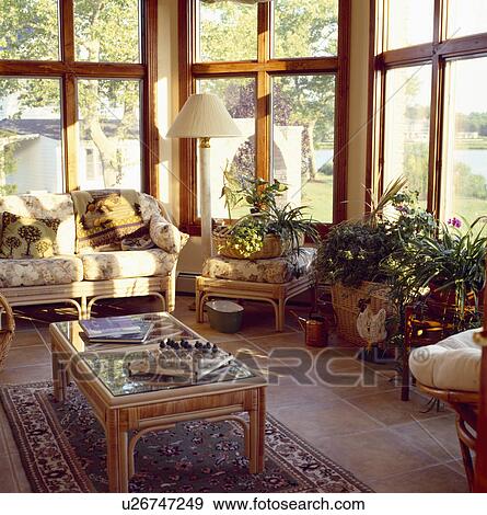 Stock Photo - Conservatory livingroom with floral cushions on wicker sofa and chairs and chess game on coffee table. Fotosearch