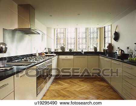 Stock Image - Contemporary cream kitchen with parquet wood floor, stainless steel extractor hood and oven. Fotosearch