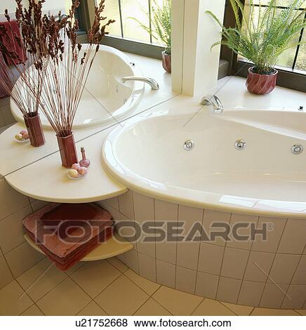 Corner-set raised bath with integral shelf in modern white bathroom with mirrored wall and white tiles View Large Photo Image Stock Photo - Corner-set raised bath with integral shelf in modern white bathroom with mirrored wall and white tiles. Fotosearch