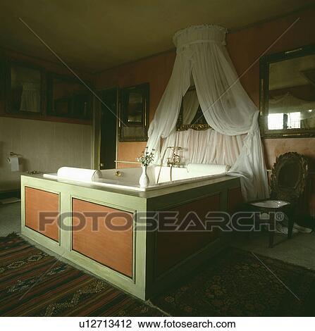 Coronet with white curtains above square white bath with green and orange panelling in traditional bathroom View Large Photo Image Stock Image - Coronet with white curtains above square white bath with green and orange panelling in traditional bathroom. Fotosearch
