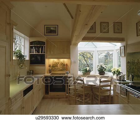 Stock Image - Country kitchen with oven in lighted alcove and small diningroom extension with circular wooden table and chairs. Fotosearch