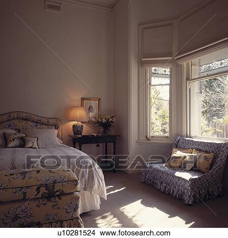 Cream linen blinds on bay window above blue+white sofa with yellow cushions in bedroom with floral ottoman View Large Photo Image Picture - Cream linen blinds on bay window above blue+white sofa with yellow cushions in bedroom with floral ottoman. Fotosearch