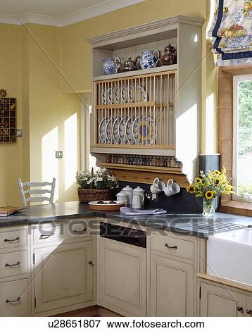 Stock Photo - Cream platerack above built-in dishwasher in pastel yellow kitchen with granite worktops on cream fitted cupboards. Fotosearch