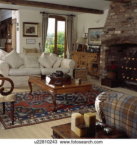 Stock Image - Cream sofa and wooden coffee table in cottage living room. Fotosearch