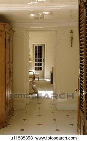Stock Image - Cream tiled floor in white hall with open doorway to living room. Fotosearch