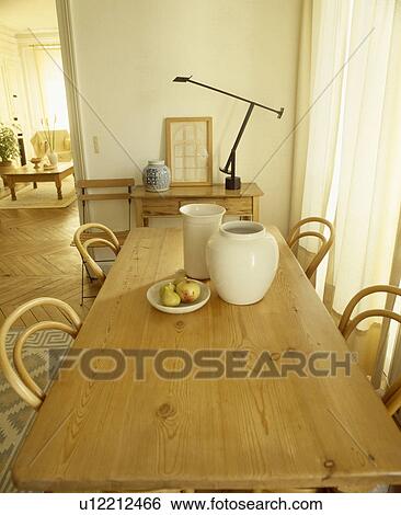 Stock Photograph - Cream vases on old pine table with bentwood chairs in neutral dining room. Fotosearch