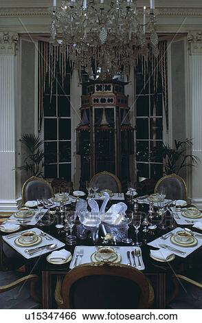 Stock Photograph - Crystal chandelier above circular table with formal place settings in large traditional dining room. Fotosearch