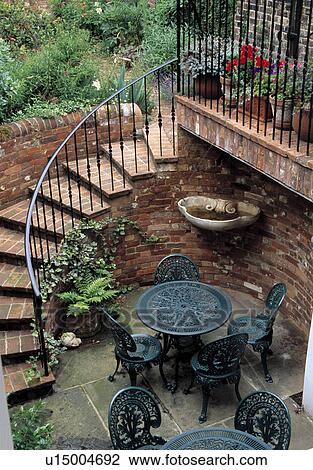 Stock Image - Curved brick sairway leading to basement patio with containers and furniture. &#13; &#10;. Fotosearch