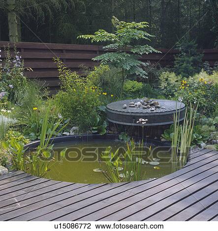 Stock Image - Decking and circular pond in country garden. Fotosearch