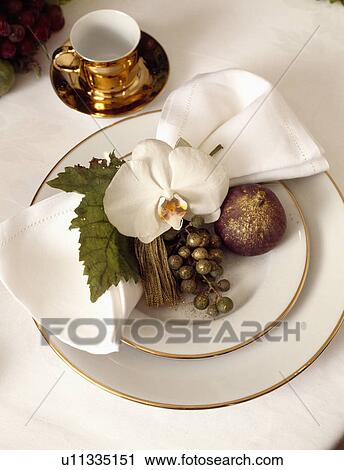 Stock Image - Detail of place setting, gold rimmed white crockery with gold and white coffee cup and white orchid napkin ring . Fotosearch