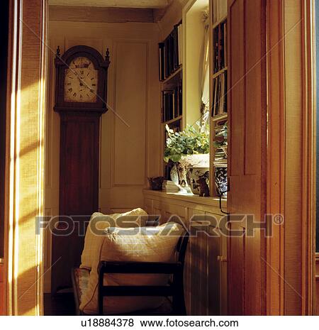 Stock Photo - Door open to antique longcase clock in small country hall with cushions on wooden chair. Fotosearch