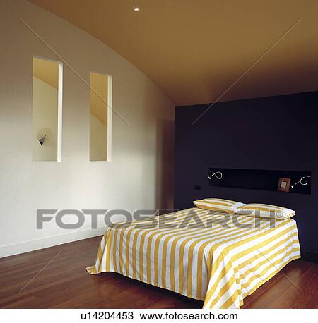 Stock Image - Double bedroom with yellow and white striped bed linen and windows through to the stairwell.. Fotosearch