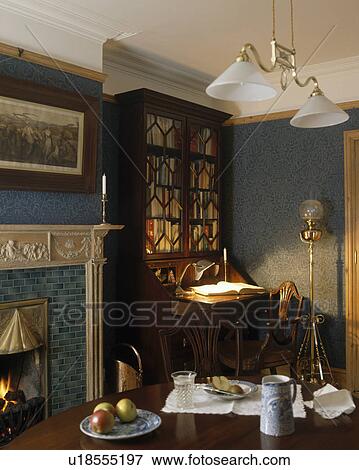 Stock Photo - Double light fitting with glass lampshades over table in diningroom with dark green wallpaper and bureau bookcase in the alcove. Fotosearch