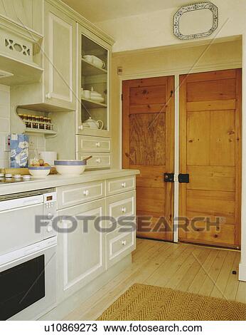 Stock Image - Double pine doors in pale grey country kitchen with white detailing on fitted cupboards. Fotosearch