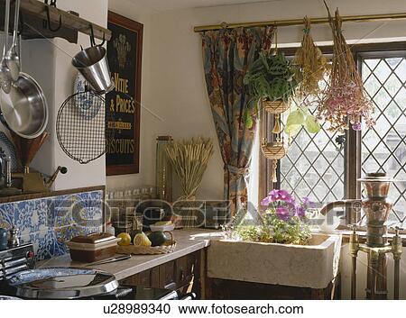 Stock Image - Dried flowers hanging above ceramic sink below lattice window in cottage kitchen. Fotosearch