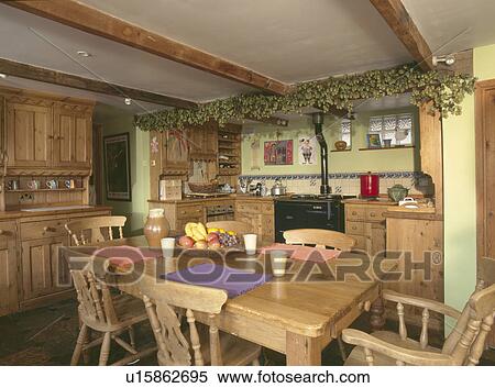 Stock Photography - Dried hop garland on ceiling beams on fitted wooden kitchen with pine table and chairs. Fotosearch