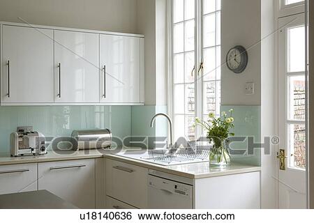 Stock Photograph - Dualit toaster and chrome breadbin on worktop below turquoise wall in modern white kitchen. Fotosearch
