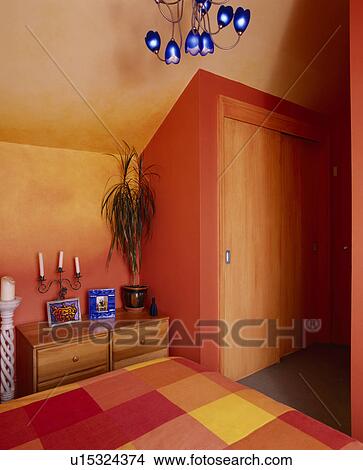 Picture - Fitted wardrobe in orange bedroom with modern blue glass light and red+yellow checked duvet on bed. Fotosearch