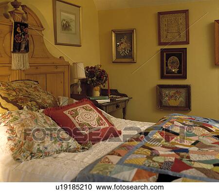 Stock Image - Floral cushions and patchwork quilt on antique pine bed in yellow country bedroom. Fotosearch