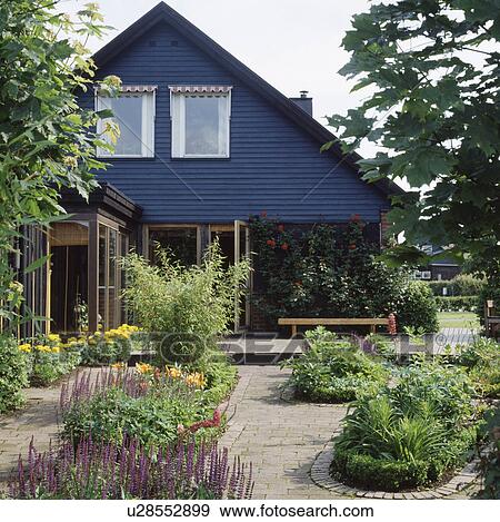 Stock Photo - Flower beds in paving in Scandinavian country garden with small blue house . Fotosearch