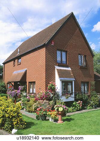 Stock Image - Flowering summer annuals in the garden on newbuild brick house. Fotosearch
