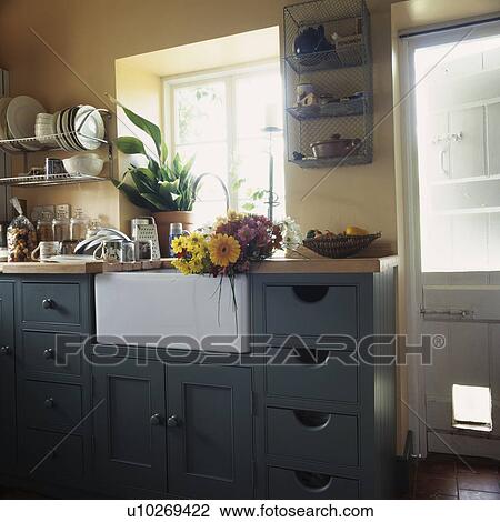 Flowers on white ceramic sink in cream kitchen with dark grey fitted cupboards with small drawers View Large Photo Image Stock Image - Flowers on white ceramic sink in cream kitchen with dark grey fitted cupboards with small drawers. Fotosearch