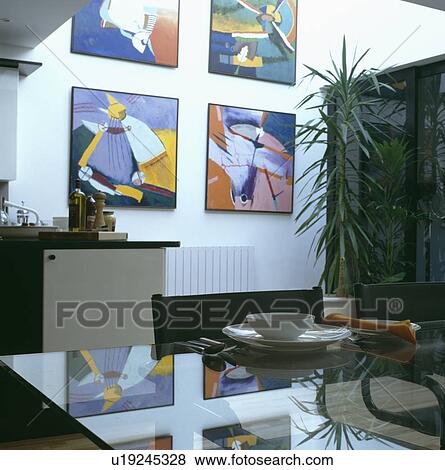 Stock Photo - Four colourful abstract paintings on white wall of eighties dining room with large houseplant and glass table. Fotosearch