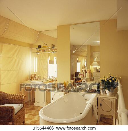 Freestanding bath below wall mirror in centre of cream bathroom with wicker armchair View Large Photo Image Stock Photograph - Freestanding bath below wall mirror in centre of cream bathroom with wicker armchair. Fotosearch
