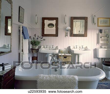 Stock Photography - Freestanding bath in white country bathroom with double basins and paenlled walls. Fotosearch