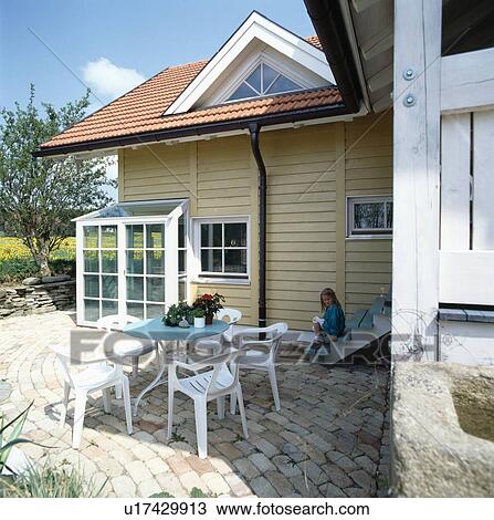 Stock Image - Furniture on patio in front of modern country house. Fotosearch