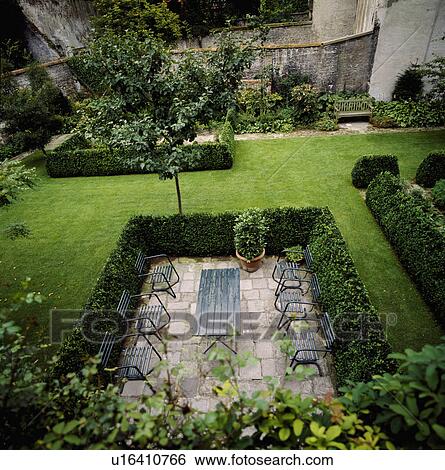 Stock Photograph - Furniture on patio within clipped hedge in country garden in summer. Fotosearch