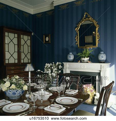 Gilt mirror above white fireplace in diningroom with blue striped wallpaper and place settings on the table View Large Photo Image Stock Image - Gilt mirror above white fireplace in diningroom with blue striped wallpaper and place settings on the table . Fotosearch