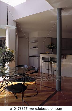 Glass and metal table and black chairs in modern kitchen with central grey pillar and wooden flooring View Large Photo Image Stock Photo - Glass and metal table and black chairs in modern kitchen with central grey pillar and wooden flooring. Fotosearch