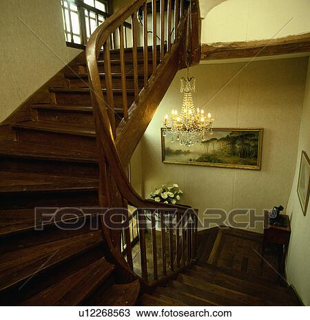 Stock Image - Glass chandelier above wooden staircase on cream landing. Fotosearch