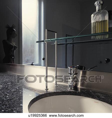 Glass perfume bottle on glass and steel shelf above underset basin in modern black granite vanity unit View Large Photo Image Stock Photograph - Glass perfume bottle on glass and steel shelf above underset basin in modern black granite vanity unit. Fotosearch