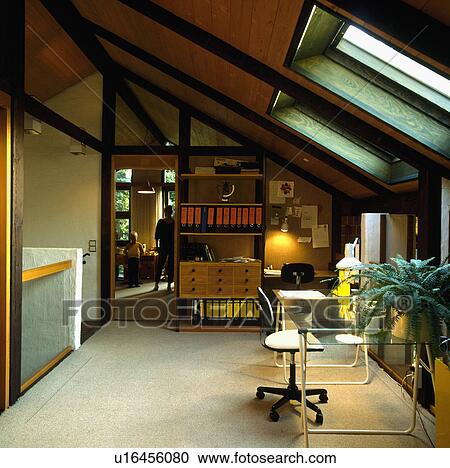 Stock Image - Glass-topped table in homeoffice in converted attic with wall of shelves and storage and cream carpet. Fotosearch