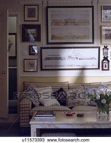 Stock Image - Group of pictures on wall above checked sofa in traditional living room. Fotosearch